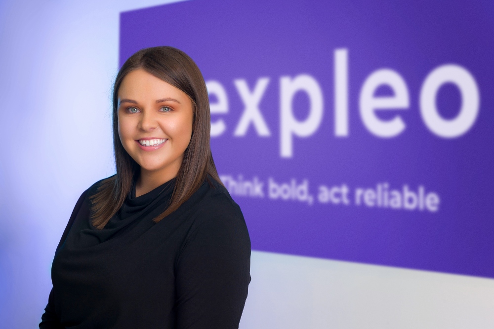 Dark-haired woman standing in front of an Expleo sign.