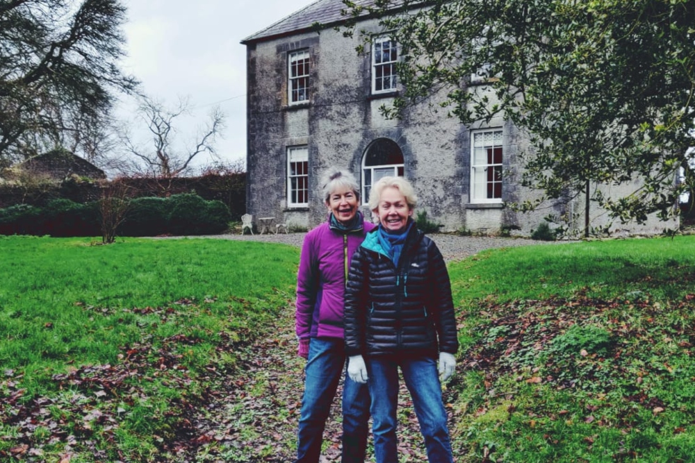 Two women standing in front of a country house.