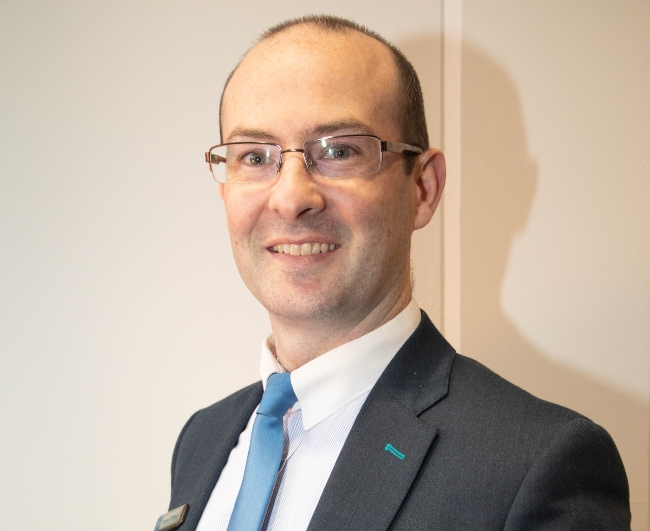 Man in glasses wearing suit with blue tie.