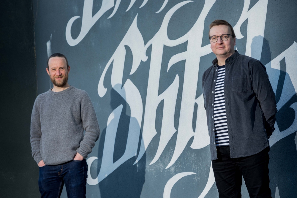 Two men standing in front of a wall.