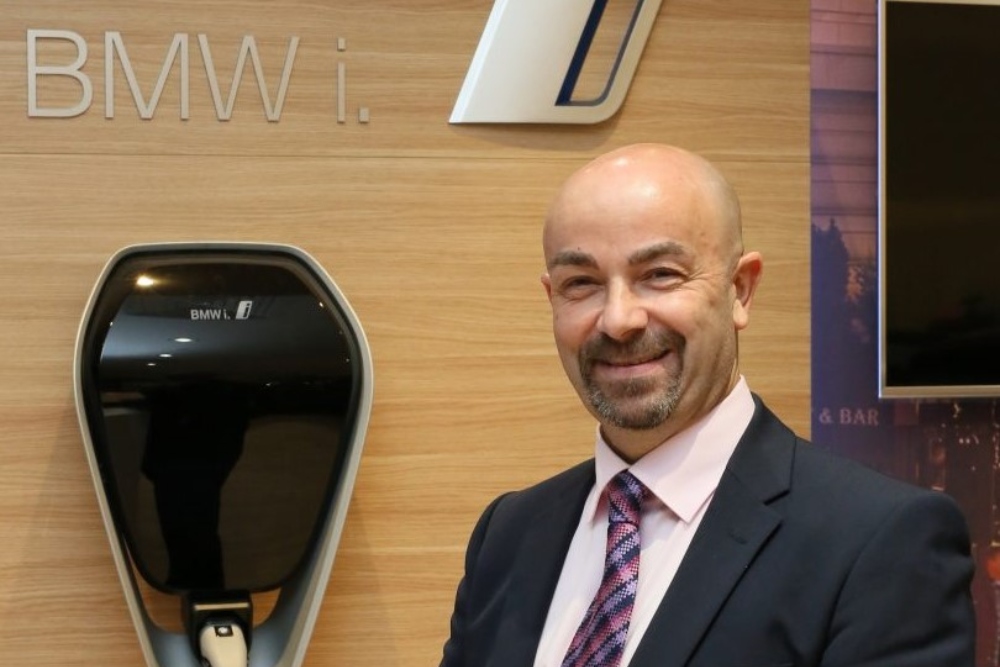 Man in suit standing beside electric car charger.