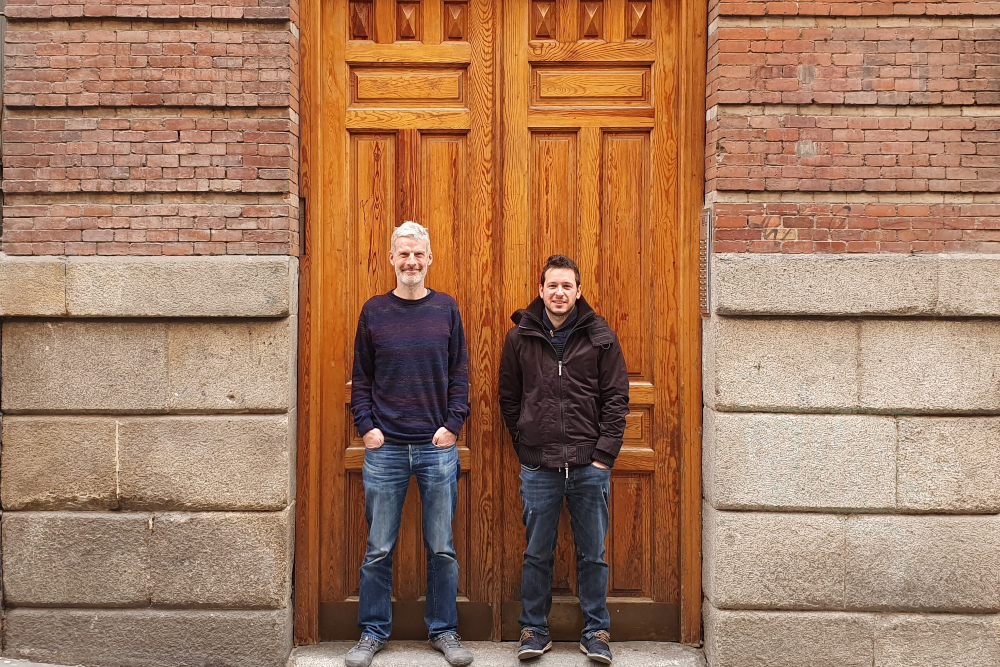 Two men standing in front of a wooden door.