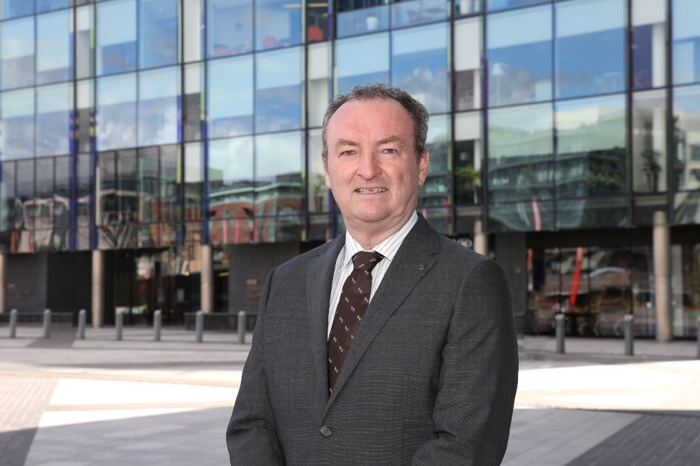 Man in suit standing in front of glass buildings.