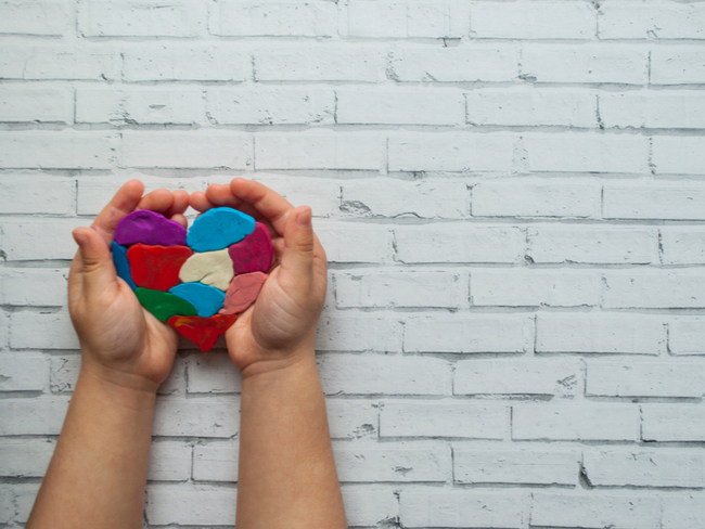 Child's hands holding a multicolored heart on white background.