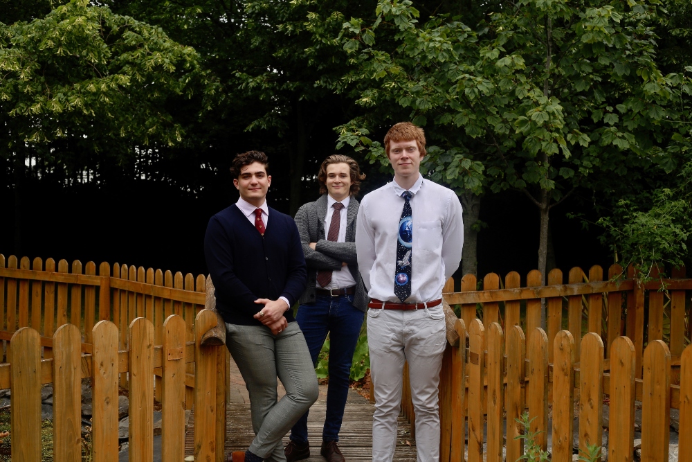 Three young male students standing at a fence.