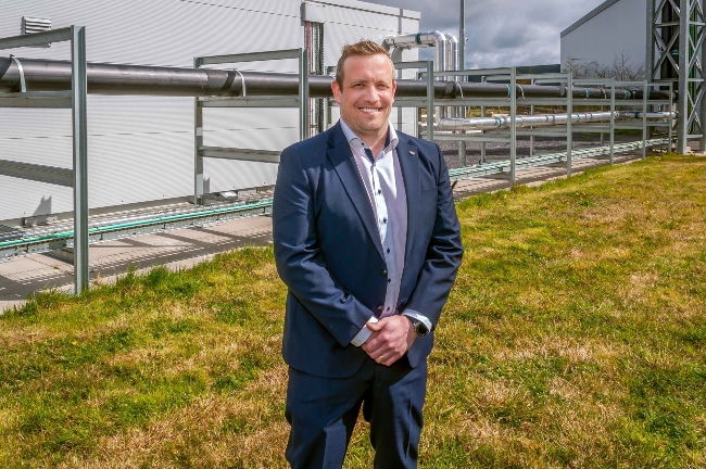 Man in blue suit standing beside industrial facility.