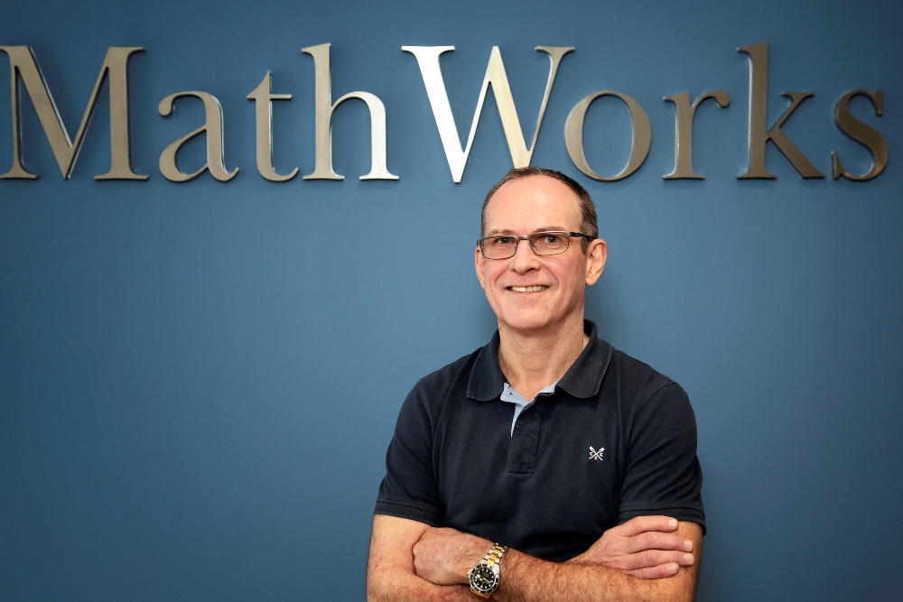 Man in black t-shirt under a sign saying MathWorks.