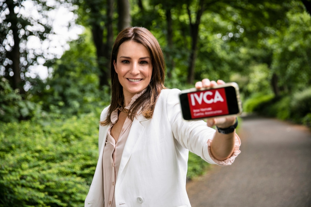 Brown haired woman in white jacket holding a smartphone.