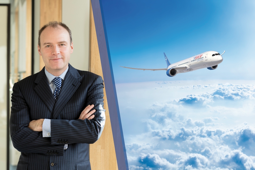 Man in suit next to image of an airplane above clouds.