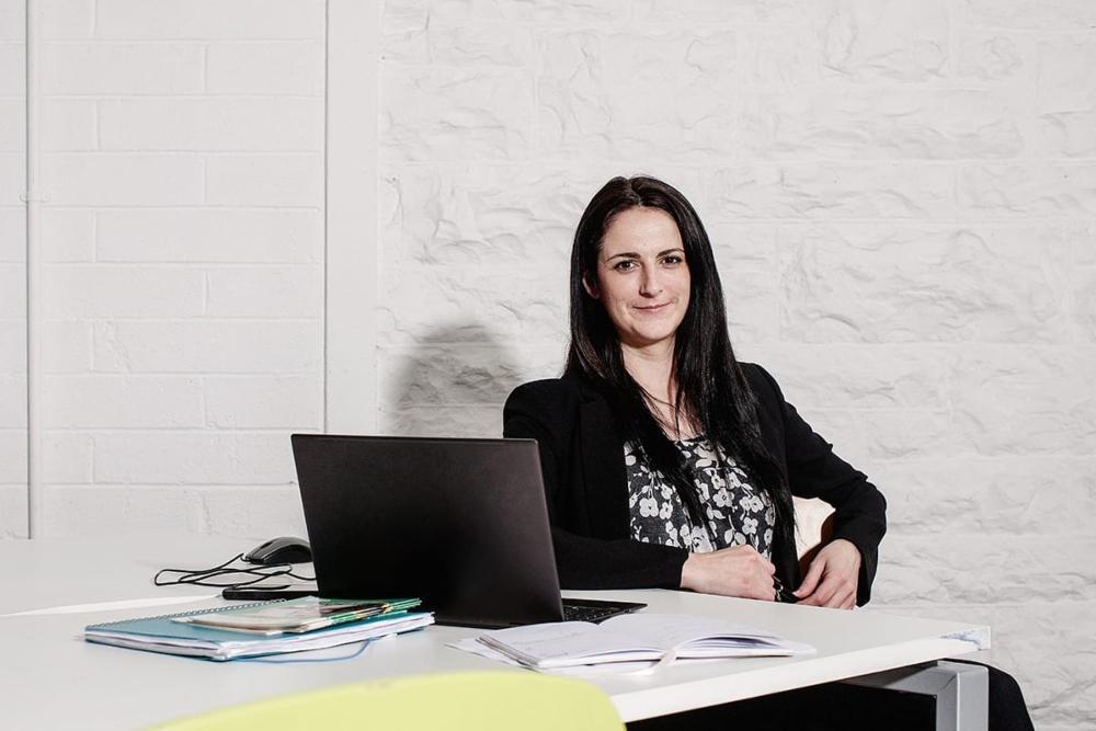 Young woman in black jacket sitting at a desk.