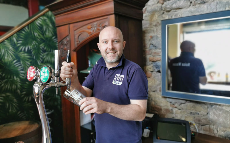 Man in blue t-shirt pouring a beer.