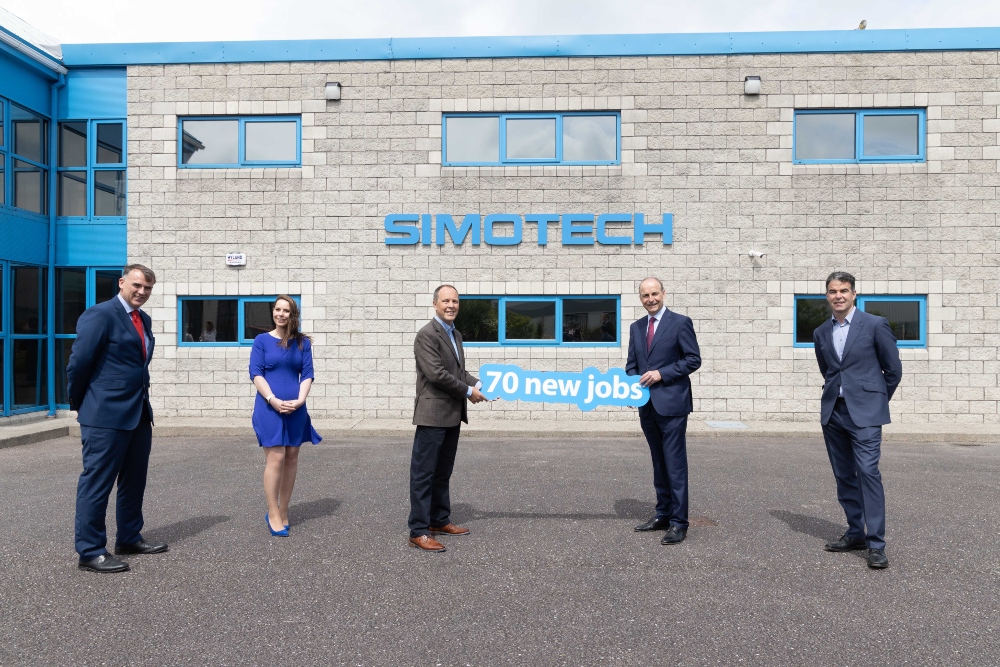 Three men and a woman outside a manufacturing building.