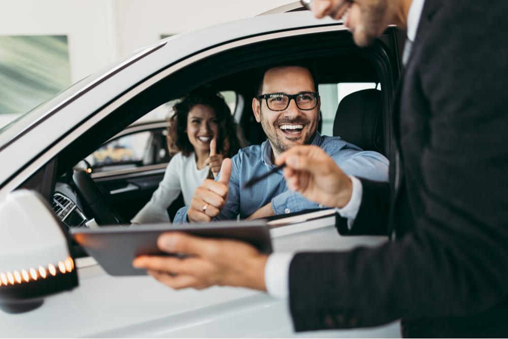 Middle age couple choosing and buying car at car showroom. Car salesman helps them to make right decision.