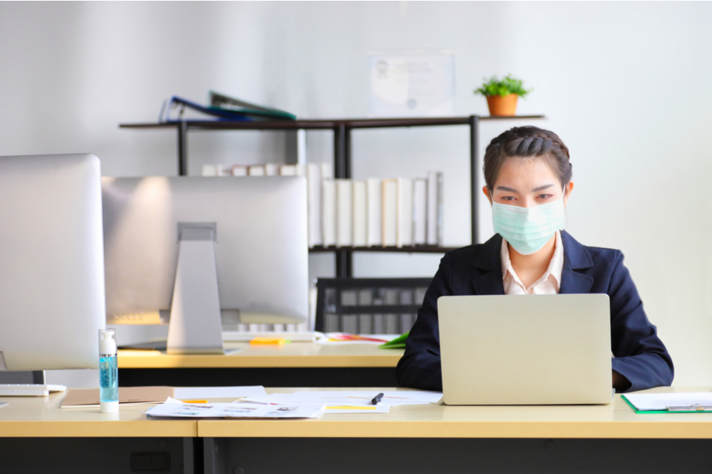 Female employee wearing medical facial mask working alone as of social distancing policy in the business office during new normal change after coronavirus or post covid-19 outbreak pandemic situation.