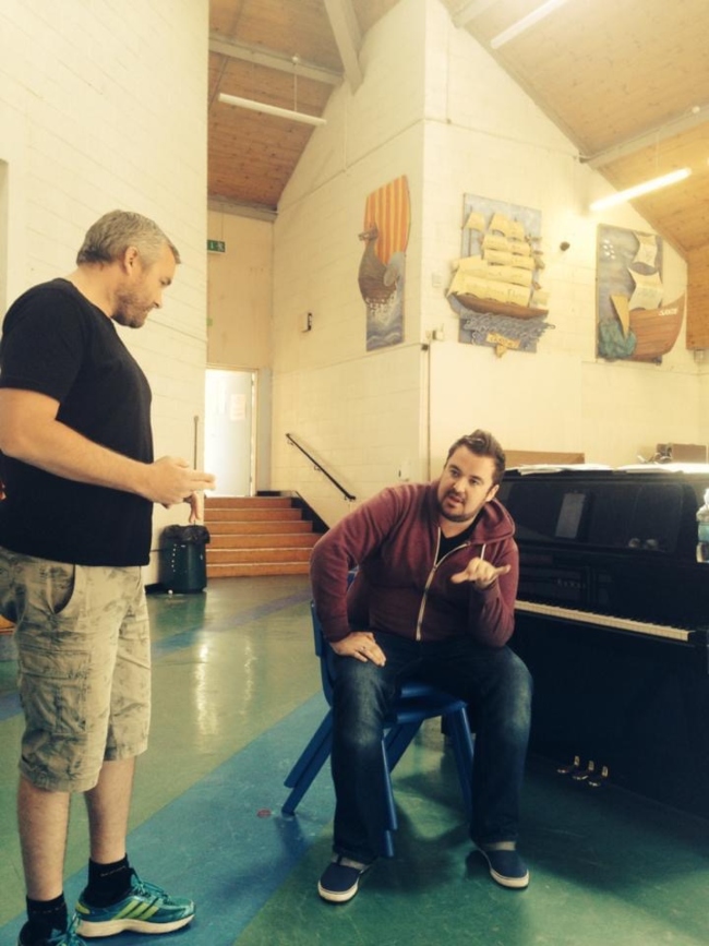 Two men talking beside piano.