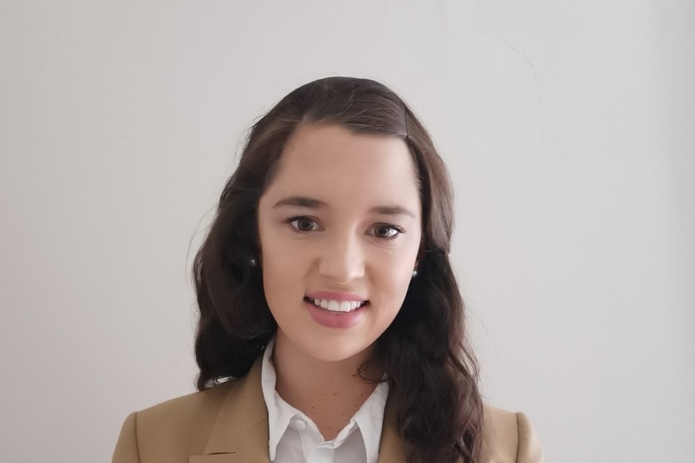 Dark-haired woman in cream jacket and white blouse.