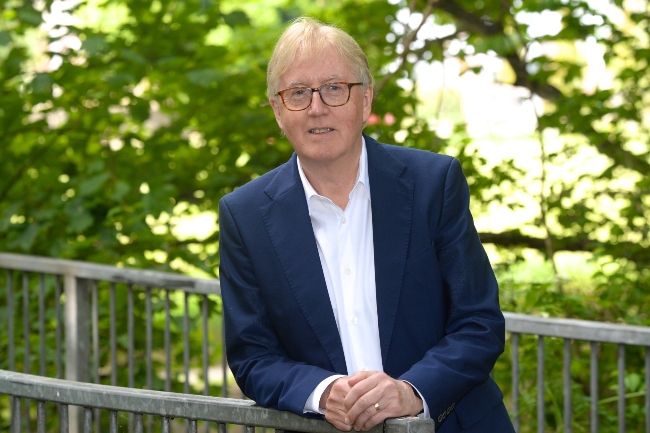 Man in blue suit leaning on fence.