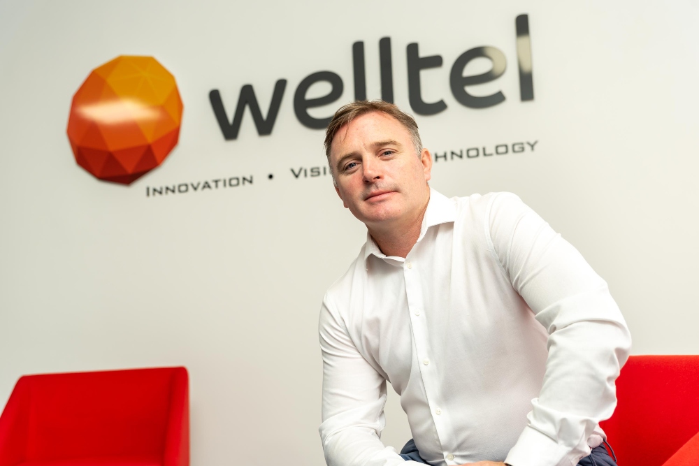 Business man in white shirt sitting under a sign saying Welltel.