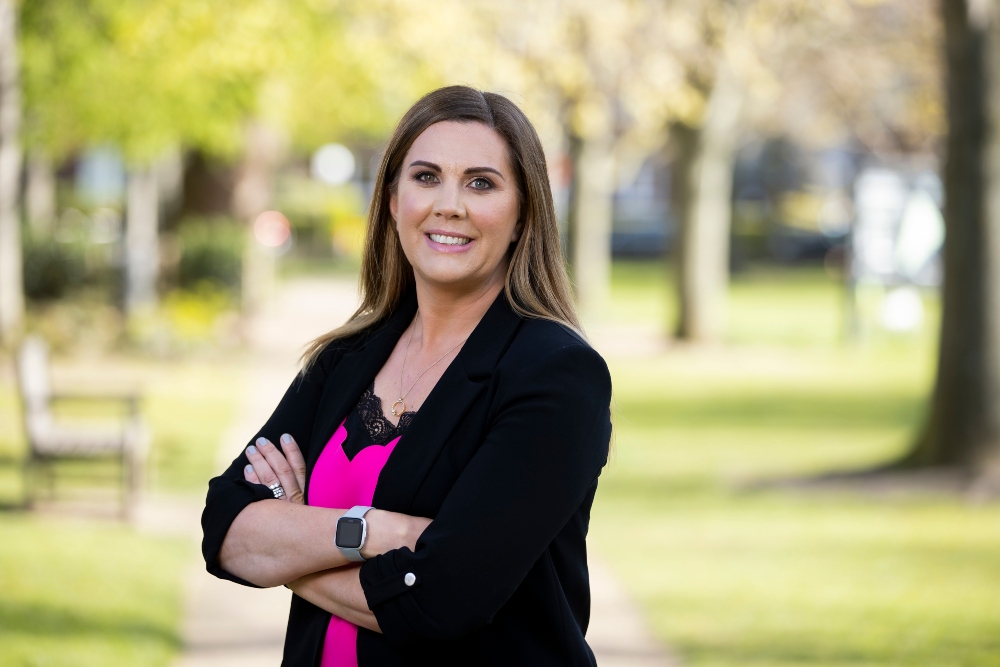 woman standing in park with arms folded.