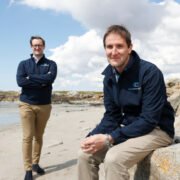 Two young men sitting on a beach.