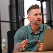Man in green t-shirt behind a MacBook.