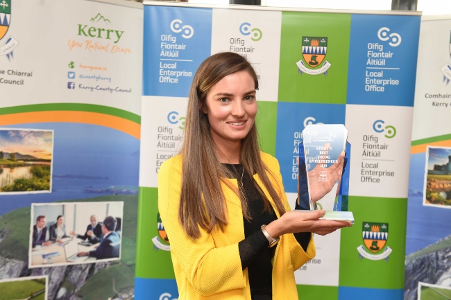 Brunette woman in yellow coat holding an award.