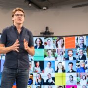 Man in black shirt speaking on a stage.