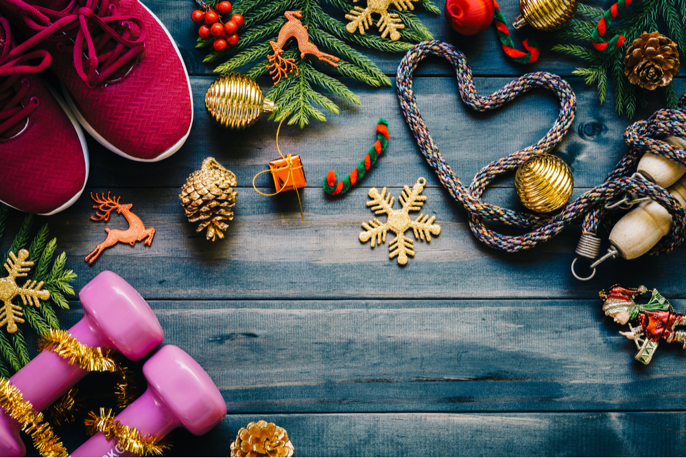 dumbbells, sport shoes, skipping rope or jump rope in heart shape with Christmas decoration items on wood background.