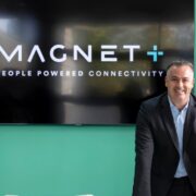 Man in grey suit in front of a green wall.