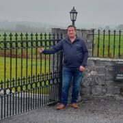 Man standing beside wrought iron gate.