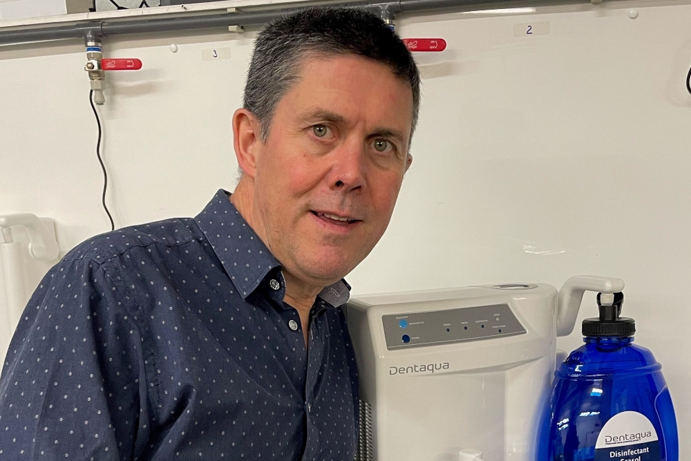 Man in grey shirt beside machine.