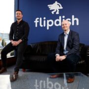 Two men sitting in front of a sign saying Flipdish.