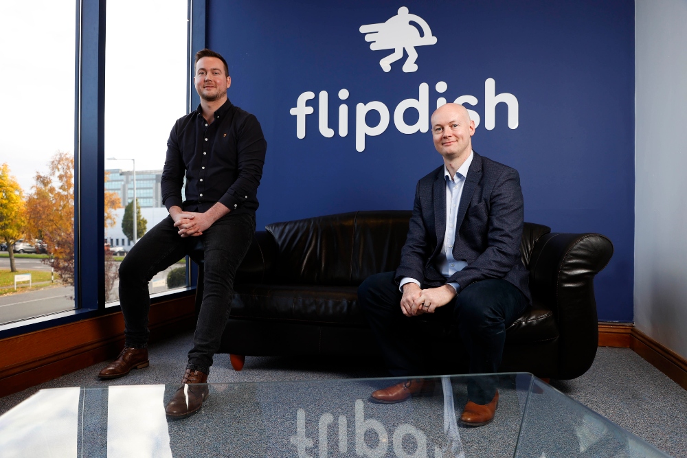 Two men sitting in front of a sign saying Flipdish.