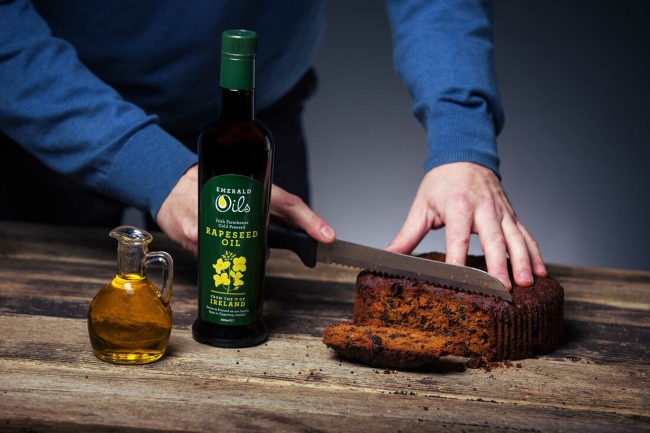 Man cutting bread beside a bottle of rapeseed oil.