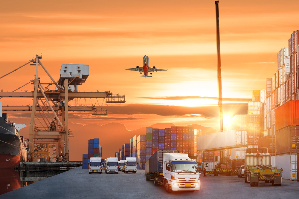 Cargo plane with working crane bridge in shipyard at sunrise.