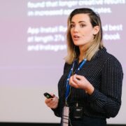 Woman speaking on stage wearing black shirt.