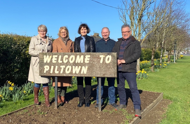 Men and women standing beside village sign for Piltown.