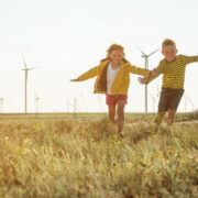 Children running in a field with wind turbines in background.