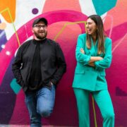 Man and woman standing in front of a colourful wall.