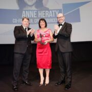 Woman in red dress beside men in black suits.