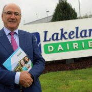 Man in suit standing in front of Lakeland Dairies sign.