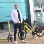 Man standing between a yellow scooter and a yellow e-bike.