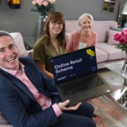 Man holding a laptop beside two women sitting on couches.