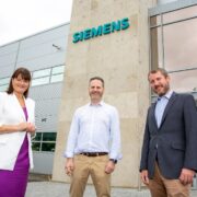 Woman and two men outside a building that has a Siemens logo on it.