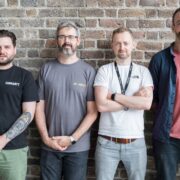 Four men in front of a brick wall.