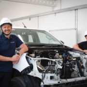 Two men in hard hats beside a jeep being reconfigured as an electric vehicle.