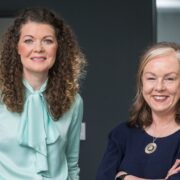 Woman in green blouse beside woman in navy blouse.