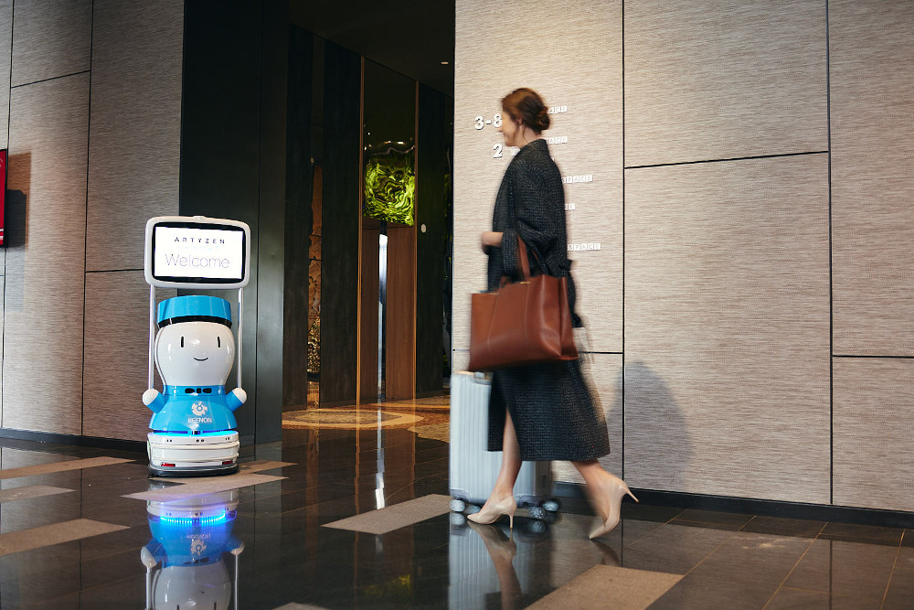 Robot greets woman in a hotel lobby.