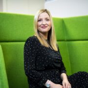 Fair haired woman sitting on green sofa.