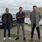 Three men with an electric car standing beside the Liffey.